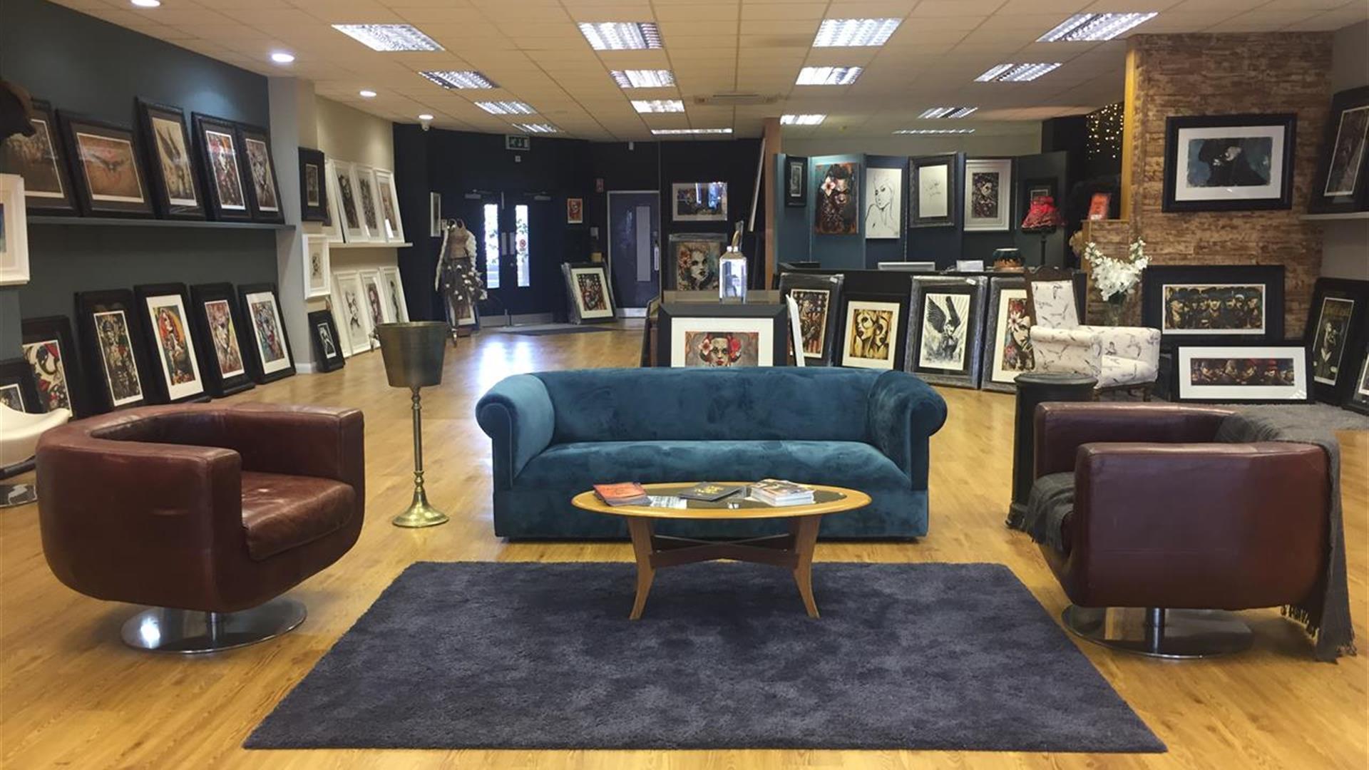 Photo of the inside of the gallery showing seating area and paintings on display for sale