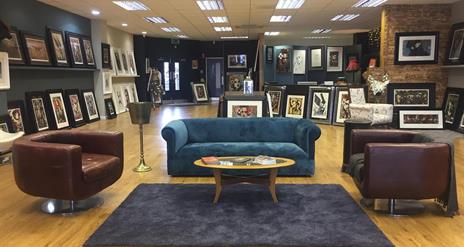 Photo of the inside of the gallery showing seating area and paintings on display for sale
