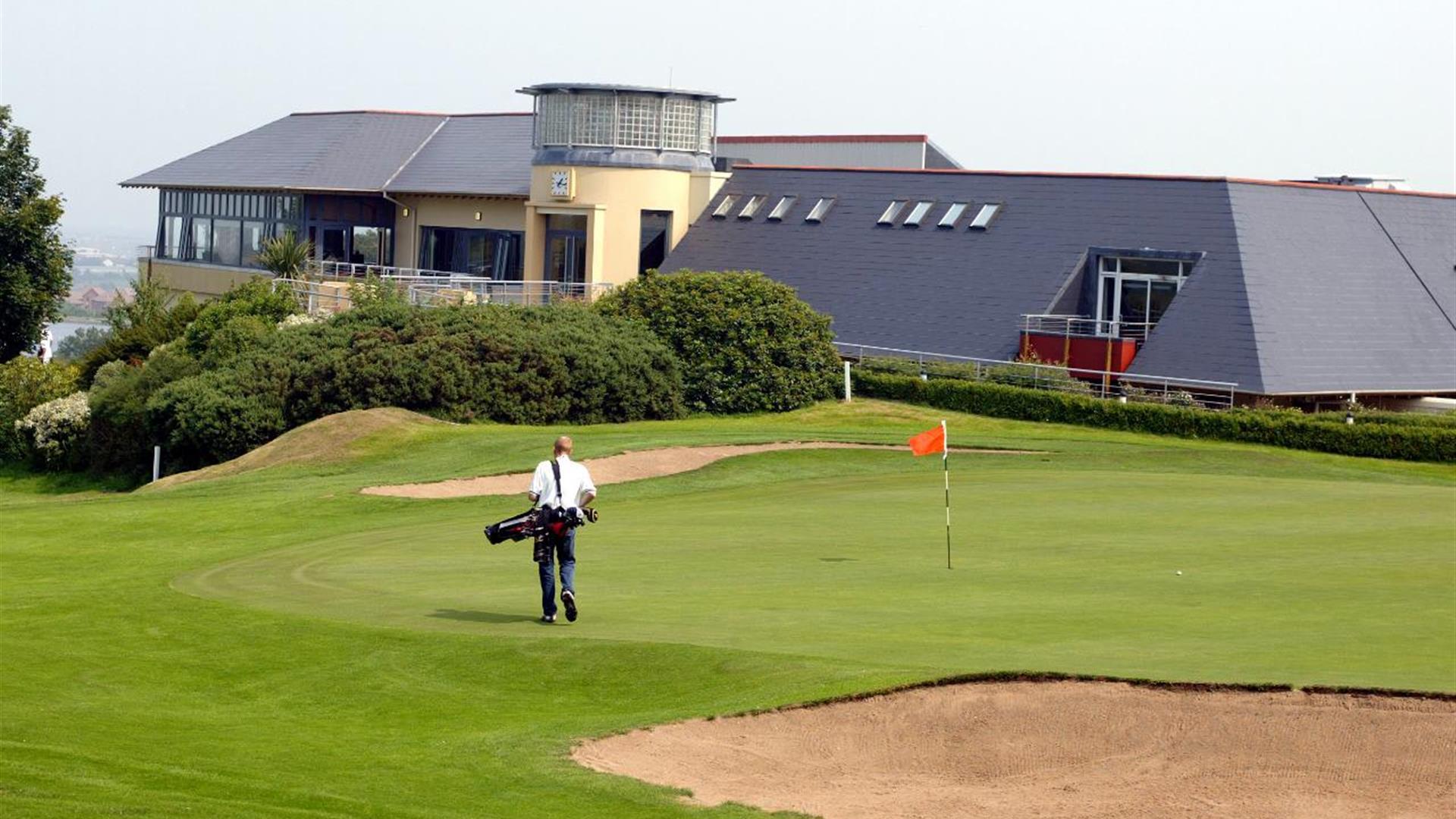 Photo of Club house and a golfer on the green to the forefront