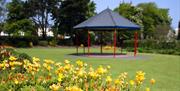 Photo of the Ward Park bandstand on a sunny day with yellow and orange flowers to forefront of image
