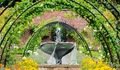 a photograph of a water fountain in the bangor walled garden surrounded by metal arches and colourful flowers