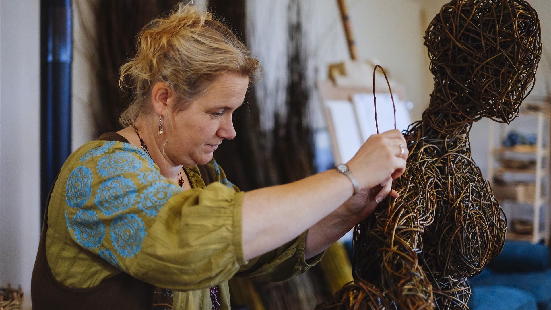A lady at work on a weaving sculpture resembling a person