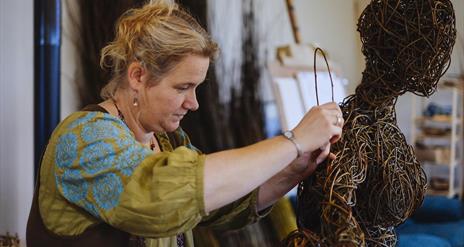 A lady at work on a weaving sculpture resembling a person