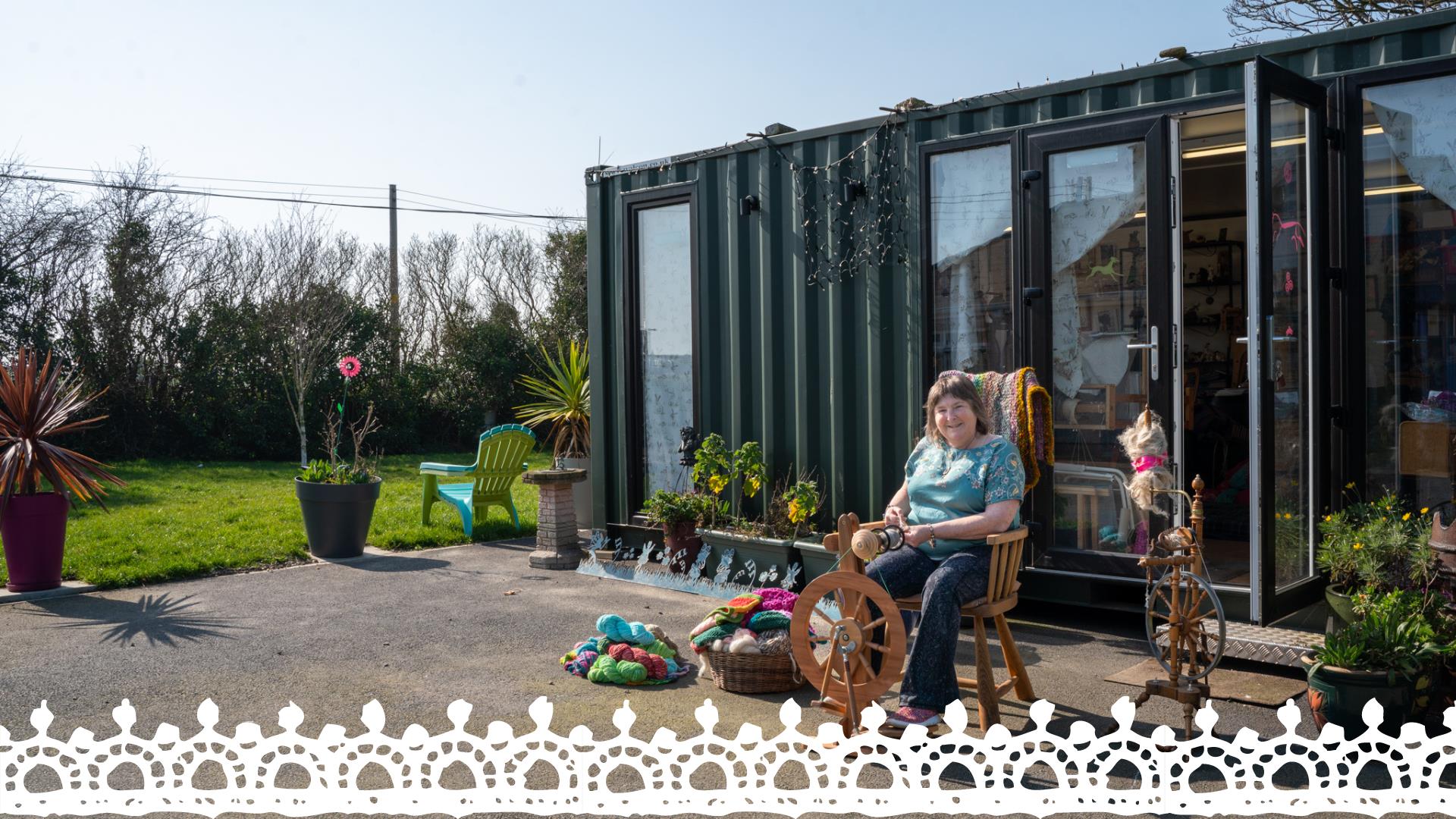 Christine of Kiri Cottage Crafts sitting outside of her workshop in front of a spinning wheel