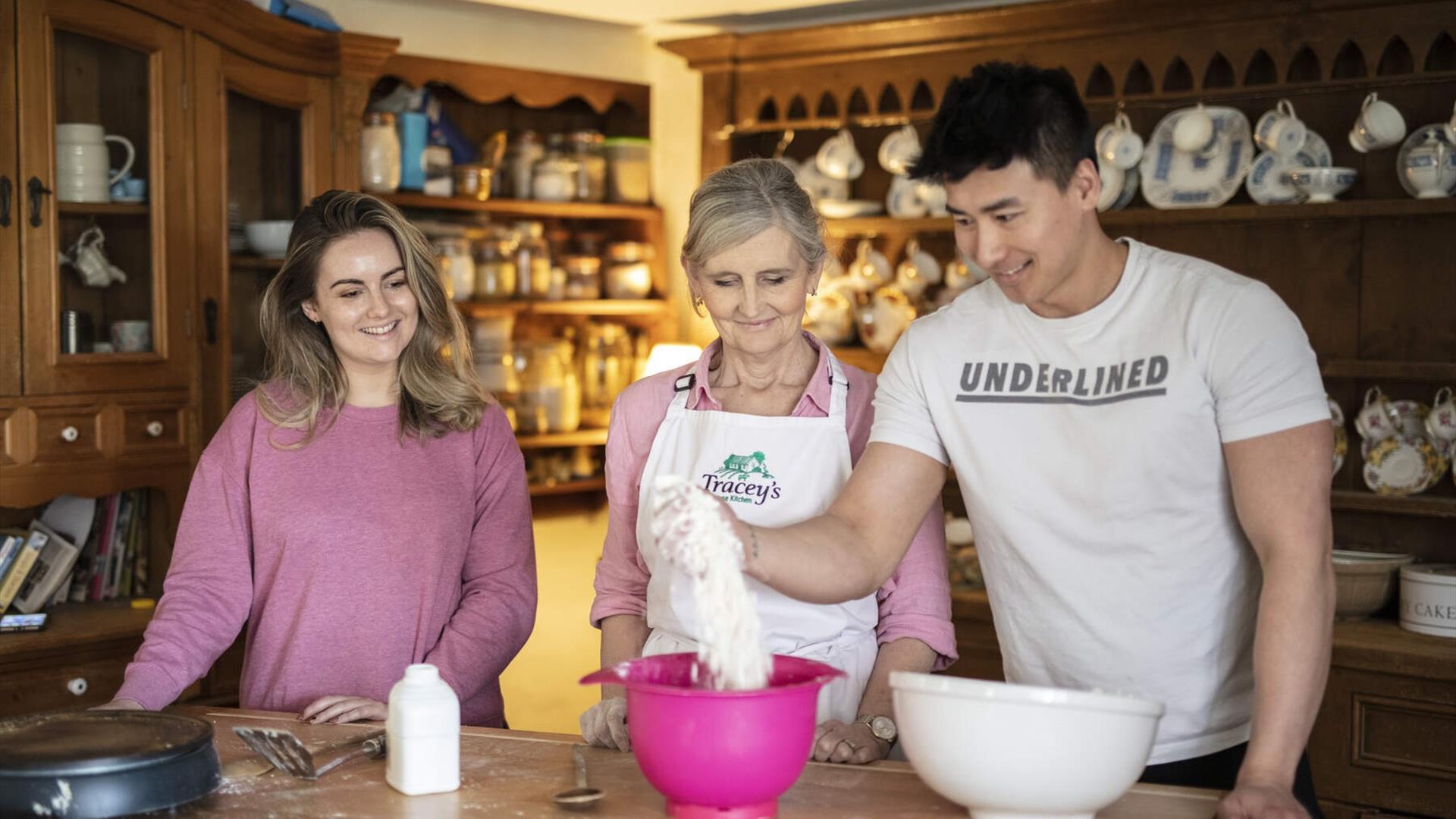 Male and female couple at kitchen table with Tracey.  The male is pouring baking flour from bag into a bowl. Male and female couple at kitchen table with Tracey.  The male is pouring baking flour from bag into a bowl.