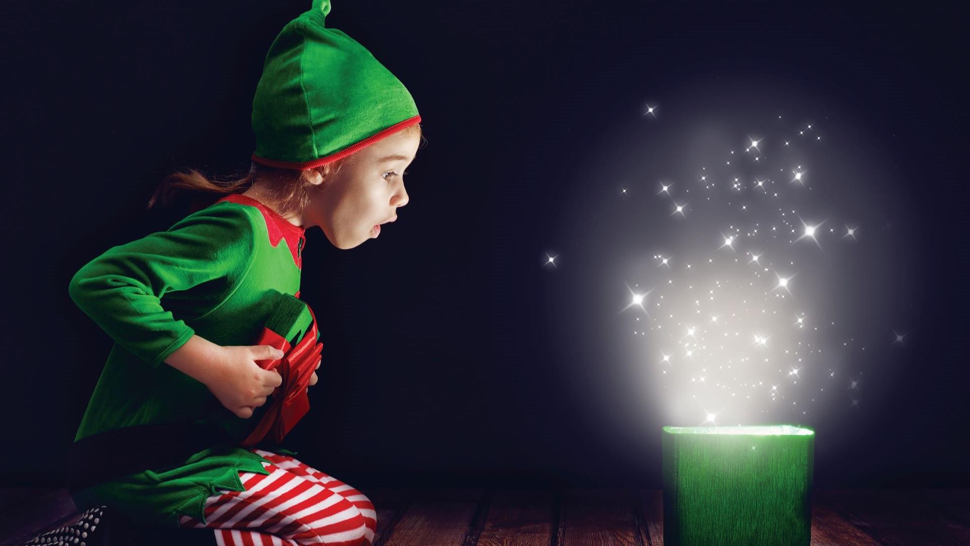 Child dressed as an elf opening a magical present.