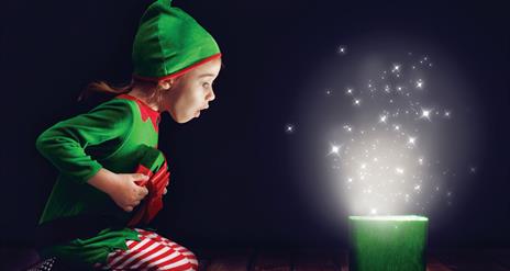 Child dressed as an elf opening a magical present.