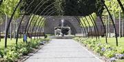 a photograph of a water fountain in the bangor walled garden surrounded by metal arches, grassy areas and paths