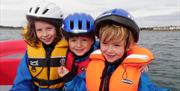 a photo of 3 kids on a boat in lifejackets