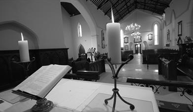 Black and white photo of from the alter of the church showing the Bible and lit candlesticks overlooking the pews