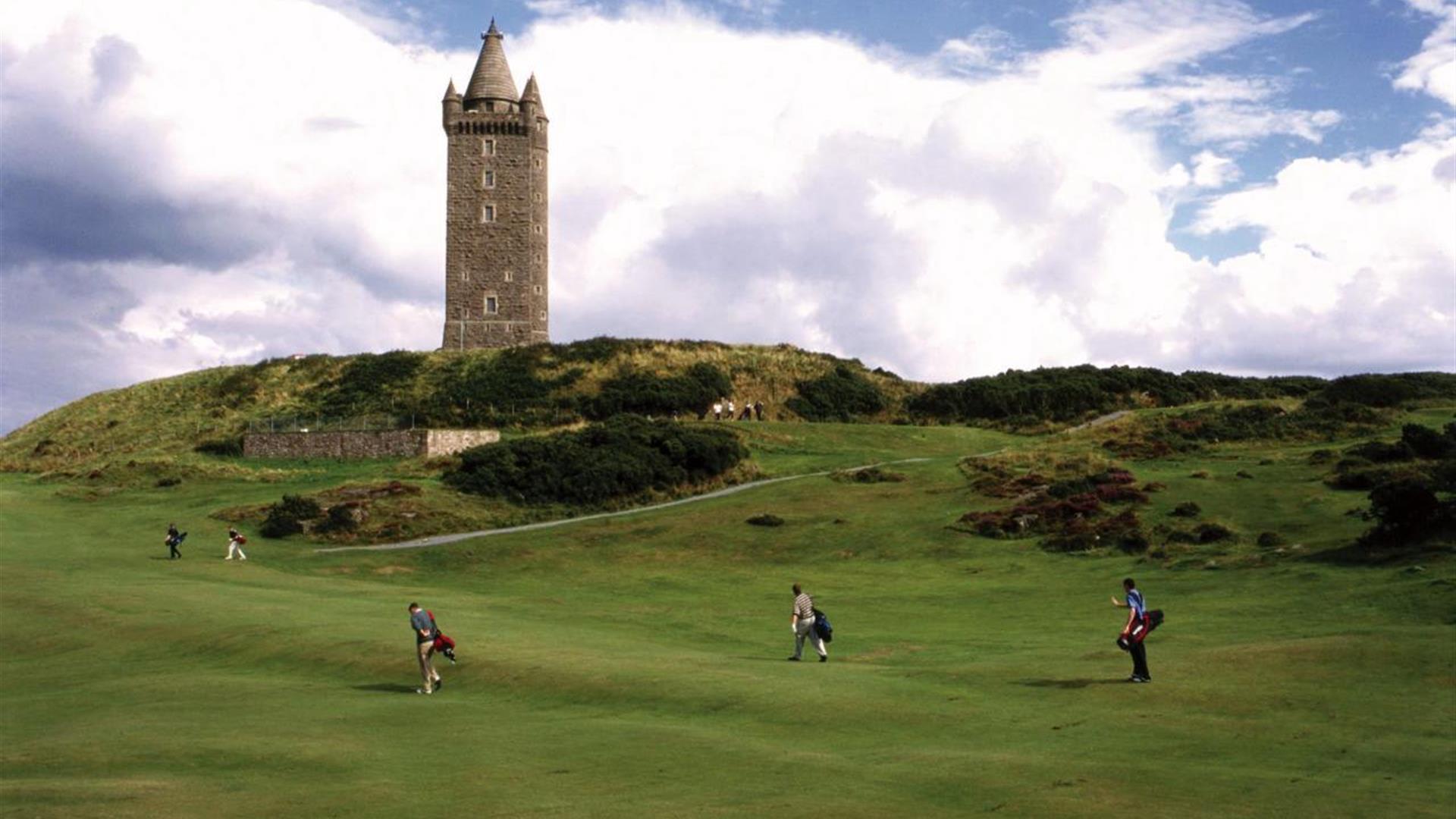 Golfers in play on the green with Scrabo Tower in background close by