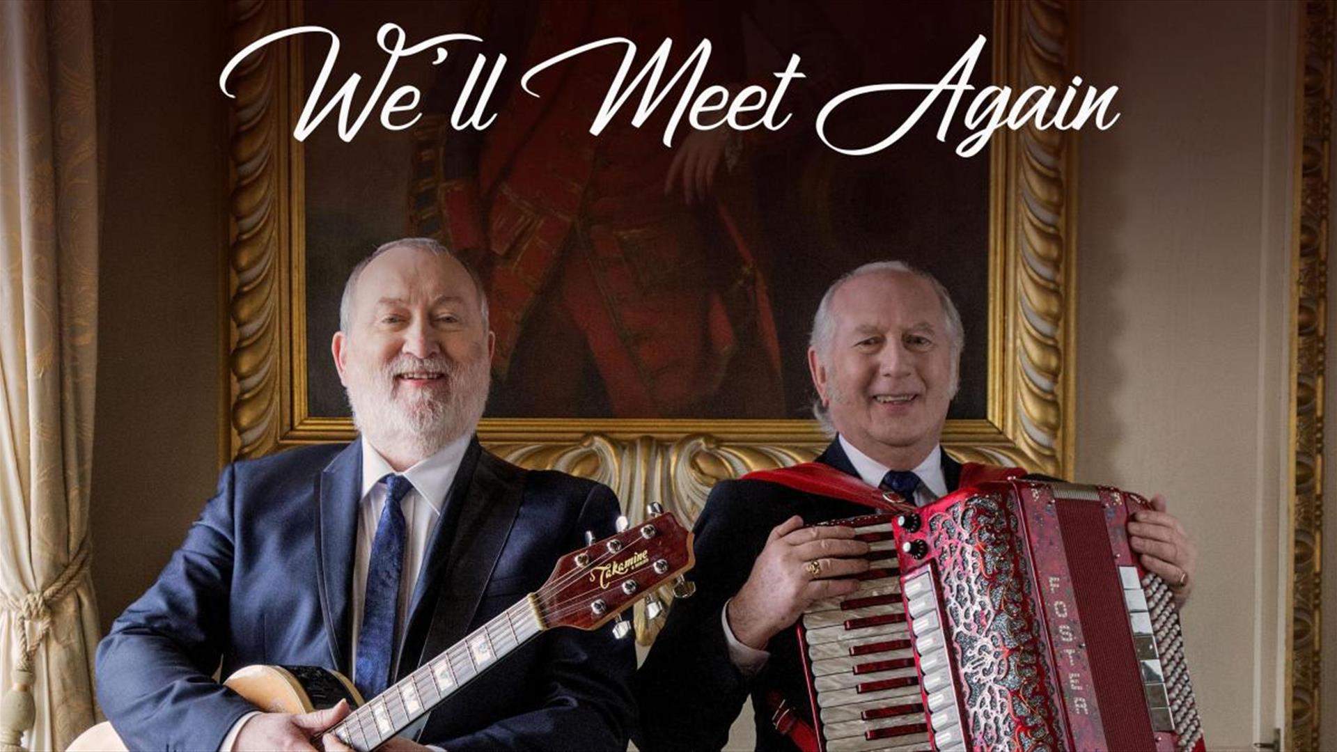 two smiling men holding an accordion and a guitar