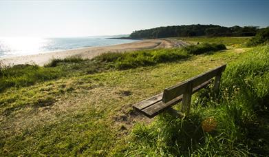 An image of Helen's Bay beach from the shore with a bench ready to welcome someone to sit