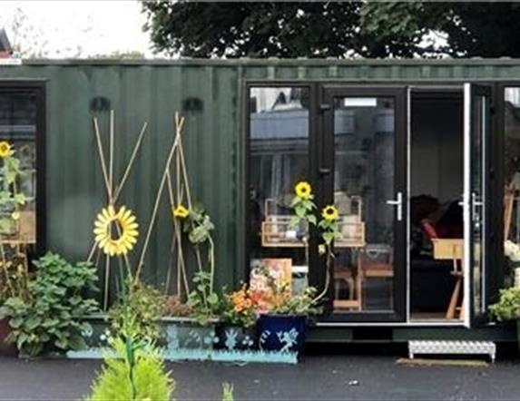 an image of an art studio made out of a storage container Sunflowers and plant containers with climbing frames outside.  View to weaving loom inside.
