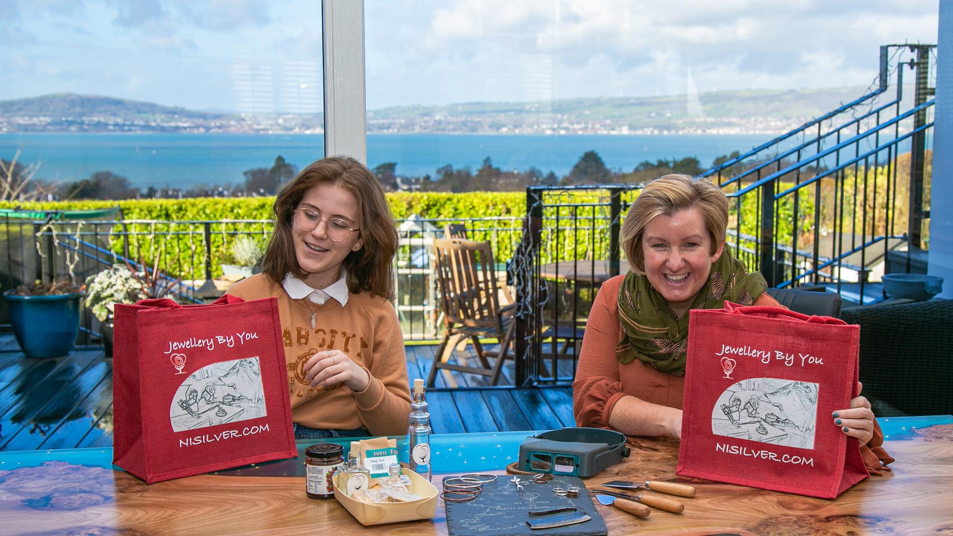 Lady and Girl Overlooking Panoramic  View of Belfast Lough from Inside House with Jewellery by You Gift Bags in Hand
