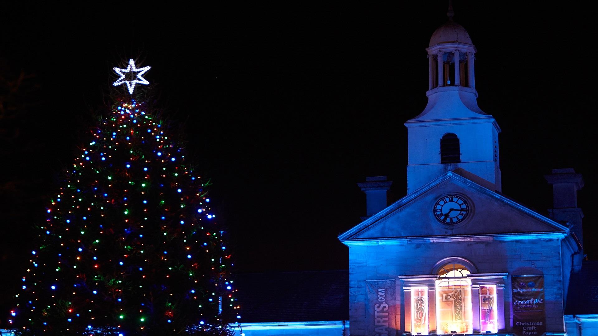 A photograph of Newtownards Christmas Tree lit at night with Ards Arts Centre in the backdrop