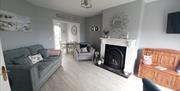 Living Room with grey 2 seater sofa and snuggle chair. Painting on wall with beach scene. Silver mirror above white fireplace. This room leads through