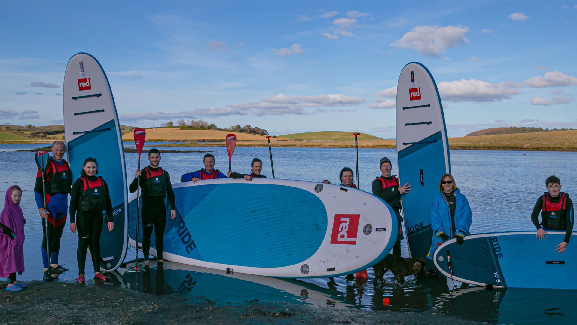 Paddleboarders of all ages standing with boards and paddles back from a session on the waters of Ballymoran Bay