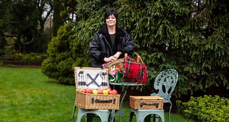 Lorraine Small of The Walled Garden Helen's Bay standing with a posh picnic hamper in the gardens.