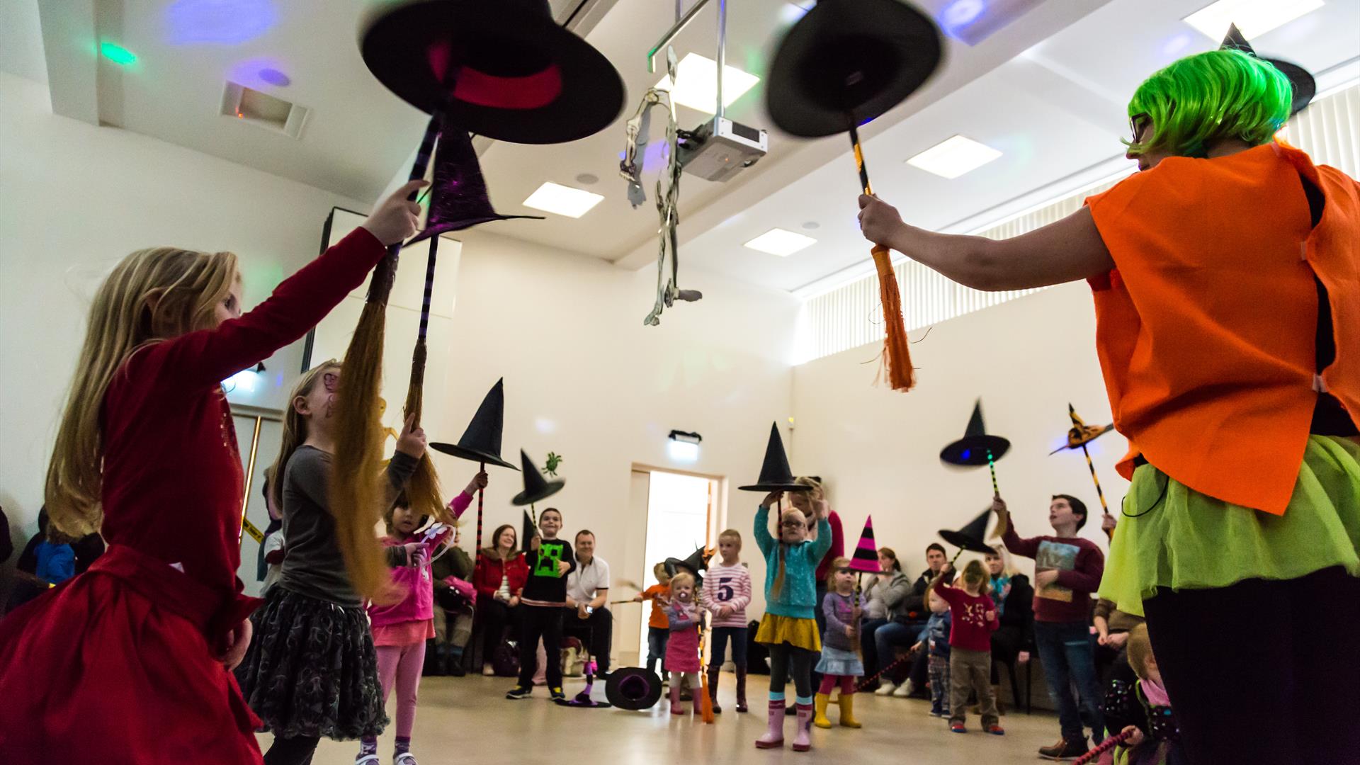 Children holding up witches hats and brooms, dressed for Hallowe'en