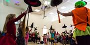 Children holding up witches hats and brooms, dressed for Hallowe'en