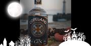 A bottle of Copeland Gin with Donaghadee Lighthouse in the background, with an overlay of spooky themed graphics for Hallowe'en