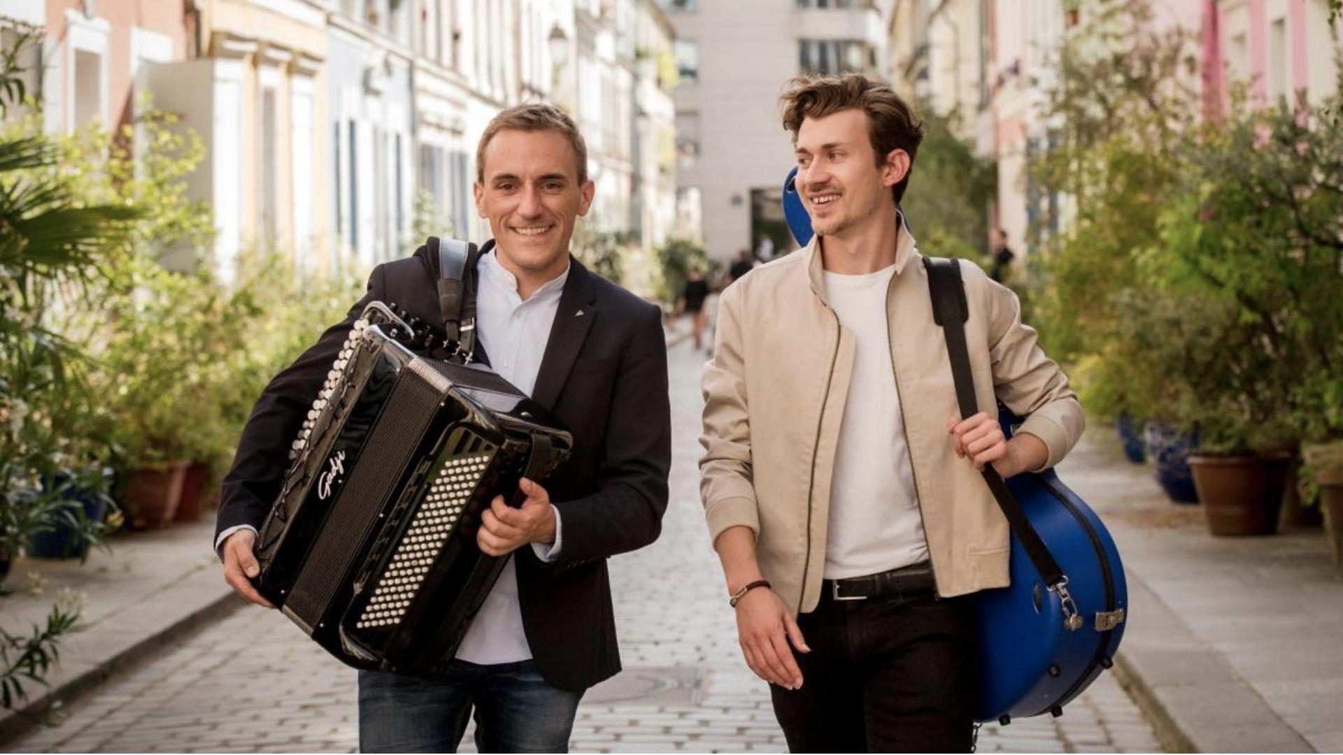 a photo of two men walking through a street holding an accordian and a guitar