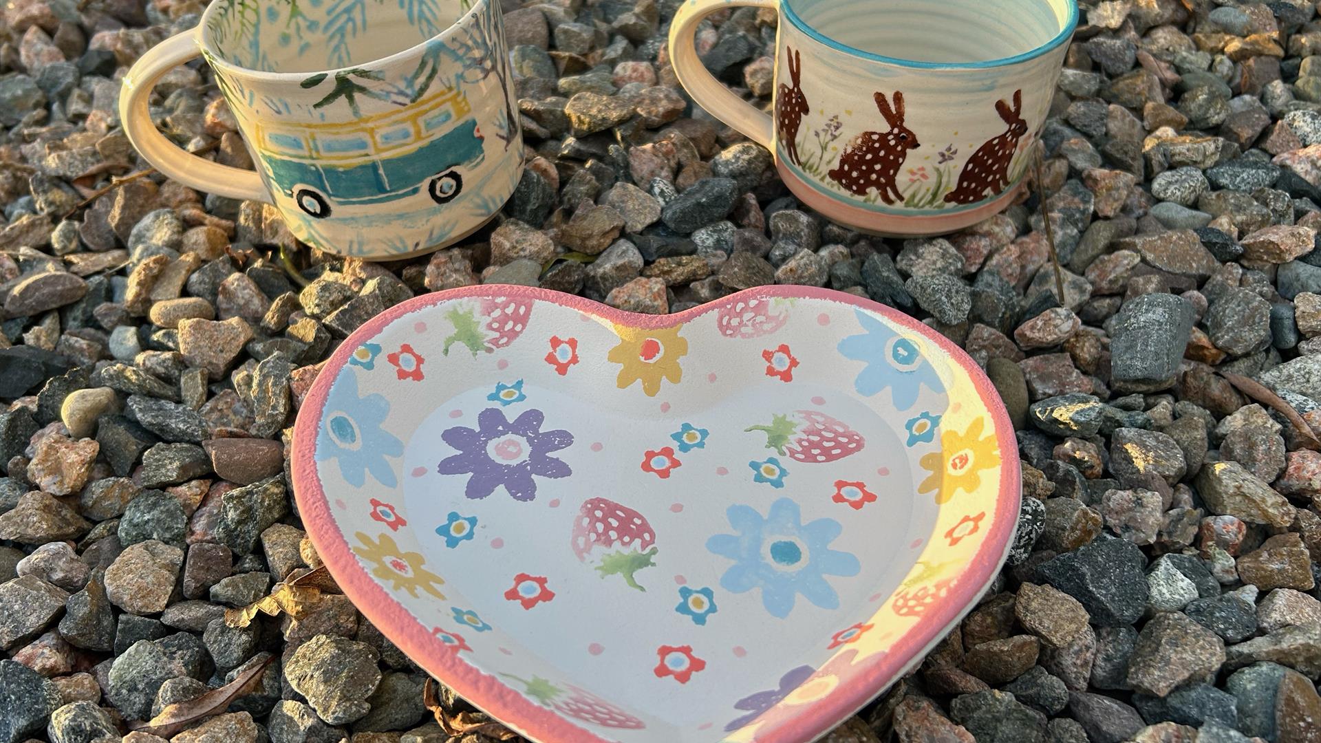 two cafe mugs decorated with a winter camper van, and little brown rabbits. A heart shaped dish sits in front of these, decorated with flowers and str