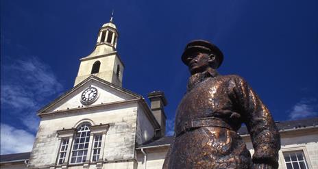 a photo of a statue in ards town square with the town hall behind